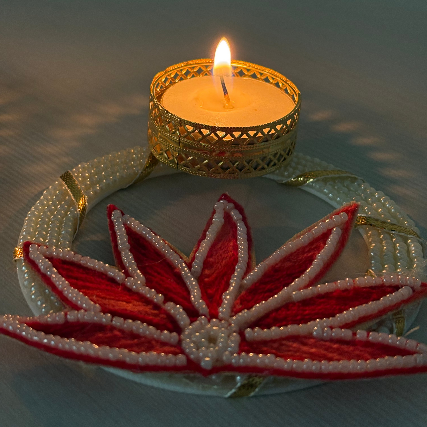 Decorative candle holder with a lit candle inside, featuring a red floral design on a light background.
