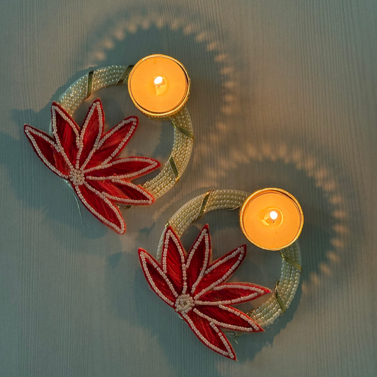 Decorative candle holders with red floral designs on a textured surface, diwali, diwali hampers, diwali diya, festive gifts, home decor, corporate gifting, diya, diyas, metallic diya, gifting, house warming gifts, 