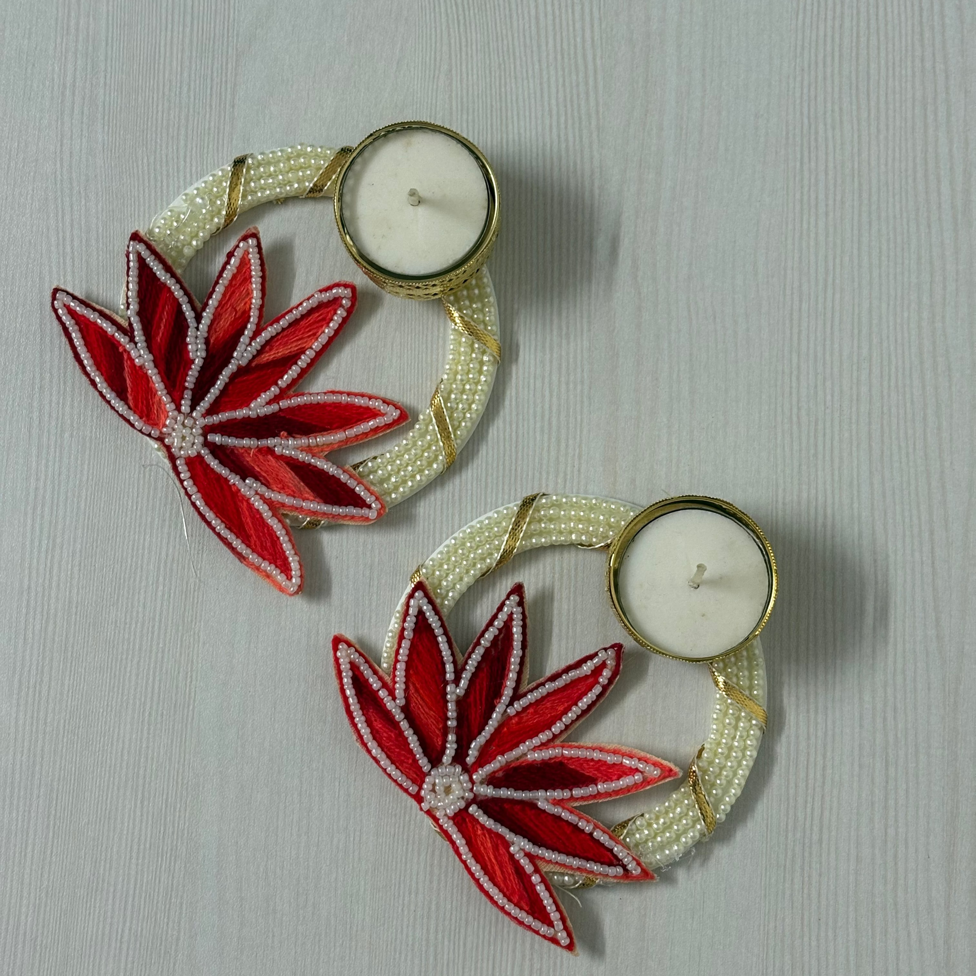 Decorative candle holders with red floral designs on a textured surface, diwali, diwali hampers, diwali diya, festive gifts, home decor, corporate gifting, diya, diyas, metallic diya, gifting, house warming gifts, 